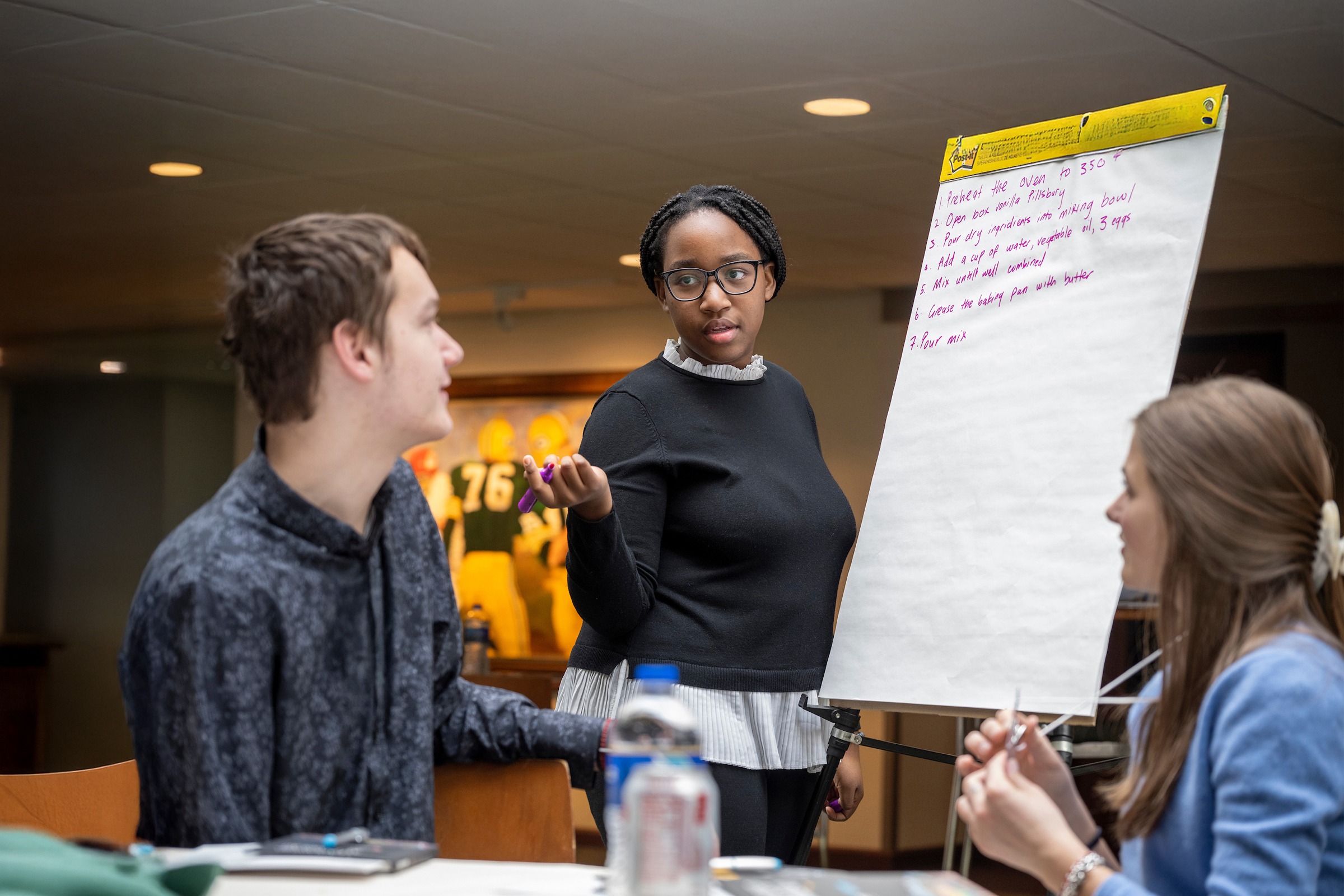 A woman with a large poster paper talking with people sitting at a table